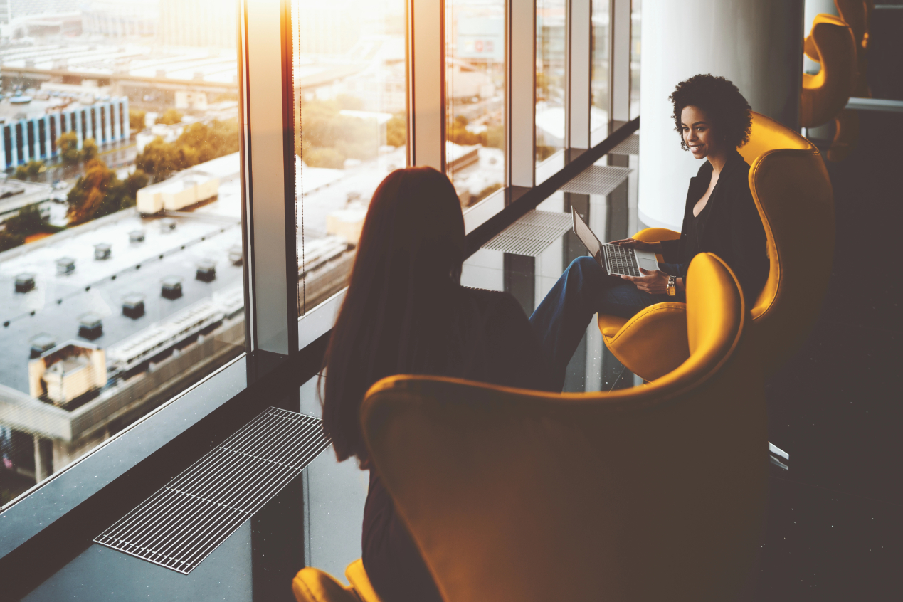 Two businesswomen having work meeting near office windows